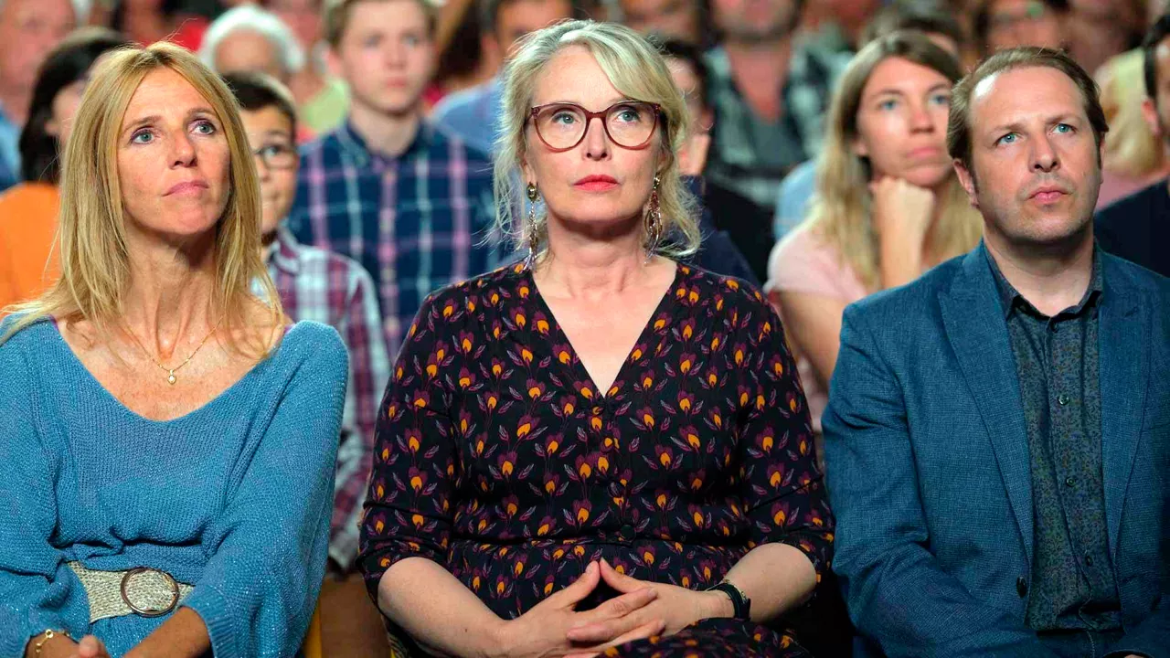 Die Supermarktbesitzerin, die Grundschullehrerin und der Bürgermeister sitzen nebeneinander im gut besuchten Bürgersaal.