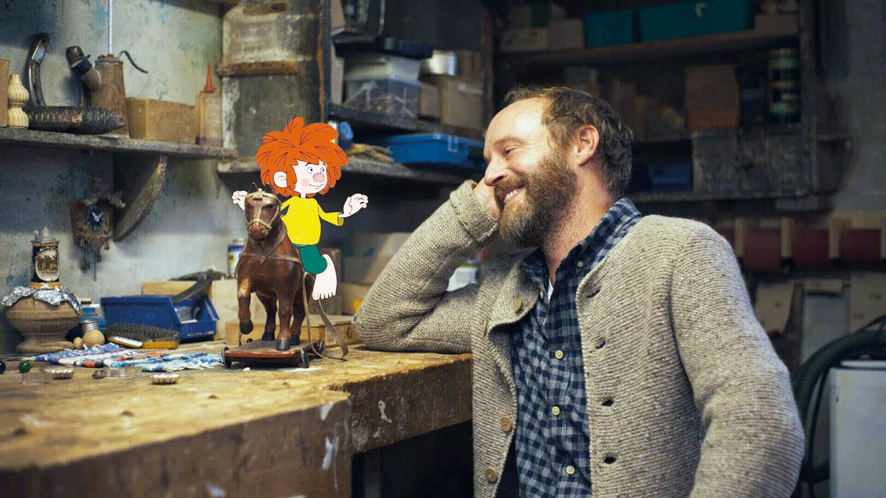 Pumuckl sitzt auf einem kleinen Holzpferd neben Meister Eder an der Werkbank.