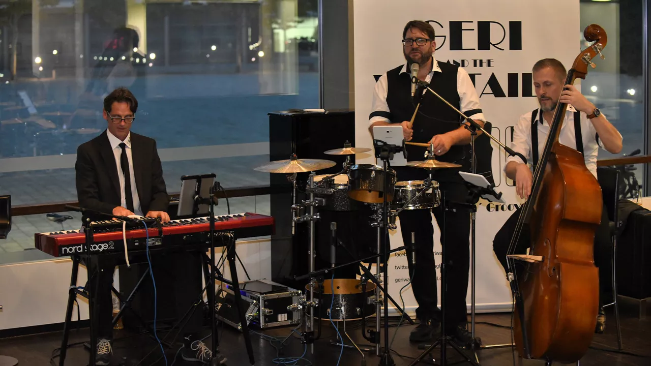 Drei Musiker spielen live: ein Mann am Keyboard, ein Schlagzeuger und ein Kontrabassist.