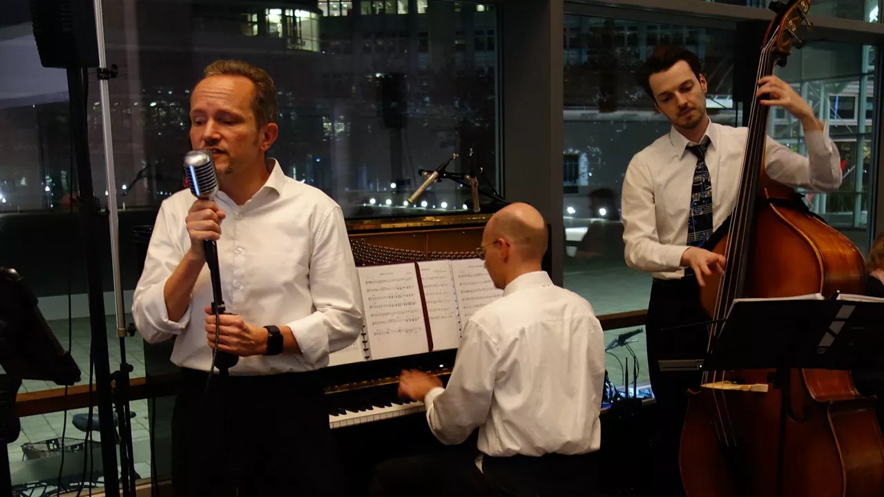 Jazztrio drinnen: Sänger mit Mikrofon, Pianist am Klavier, Bassist mit Kontrabass.