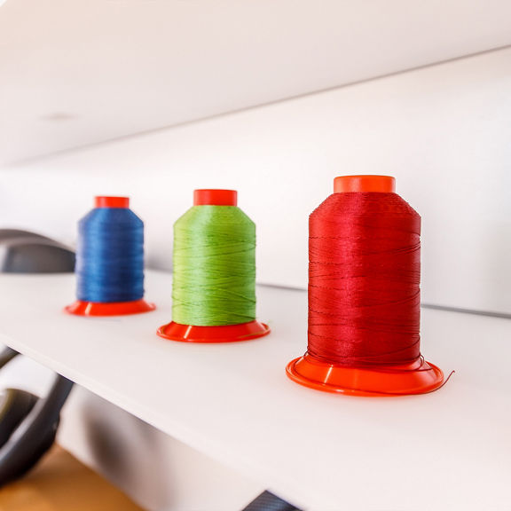 Close-up of blue, green and red spool of thread with orange base on white shelf.
