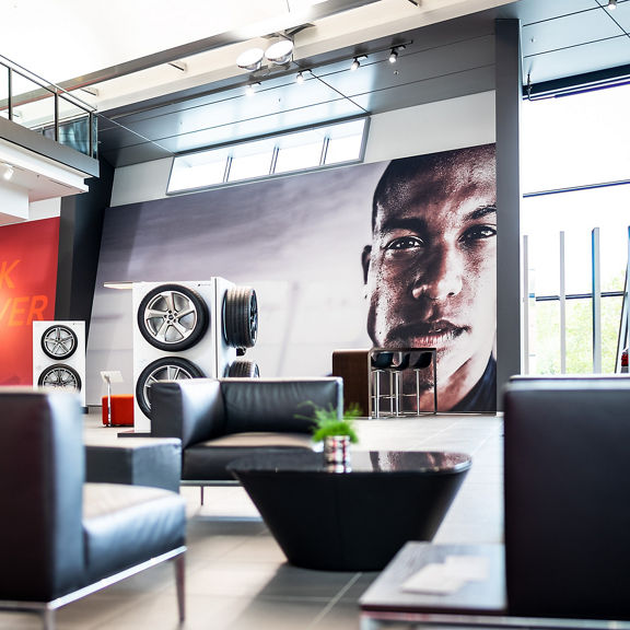 Black leather armchairs and tables in front of a large mural of a face, tire presentation in the background.
