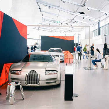 Ausstellungsraum mit mehreren Audi Modellen in verchromter Optik, Infotafeln und mehreren Besuchern im Audi Forum Neckarsulm.