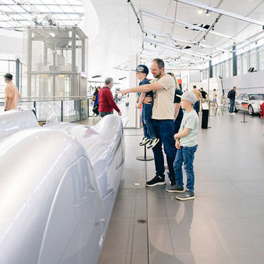 Vater mit zwei Kindern betrachtet ein Fahrzeug einer Audi Designstudie in Aluminiumoptik  in der Ausstellung im Audi Forum Neckarsulm.      