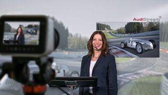 Woman with a headset stands behind the camera and we are filmed in front of a racetrack screen.