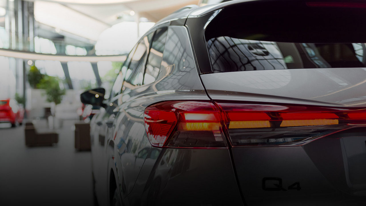 Rear view of a silver Audi Q4 in a modern showroom with light-coloured glass facades and other vehicles in the background.