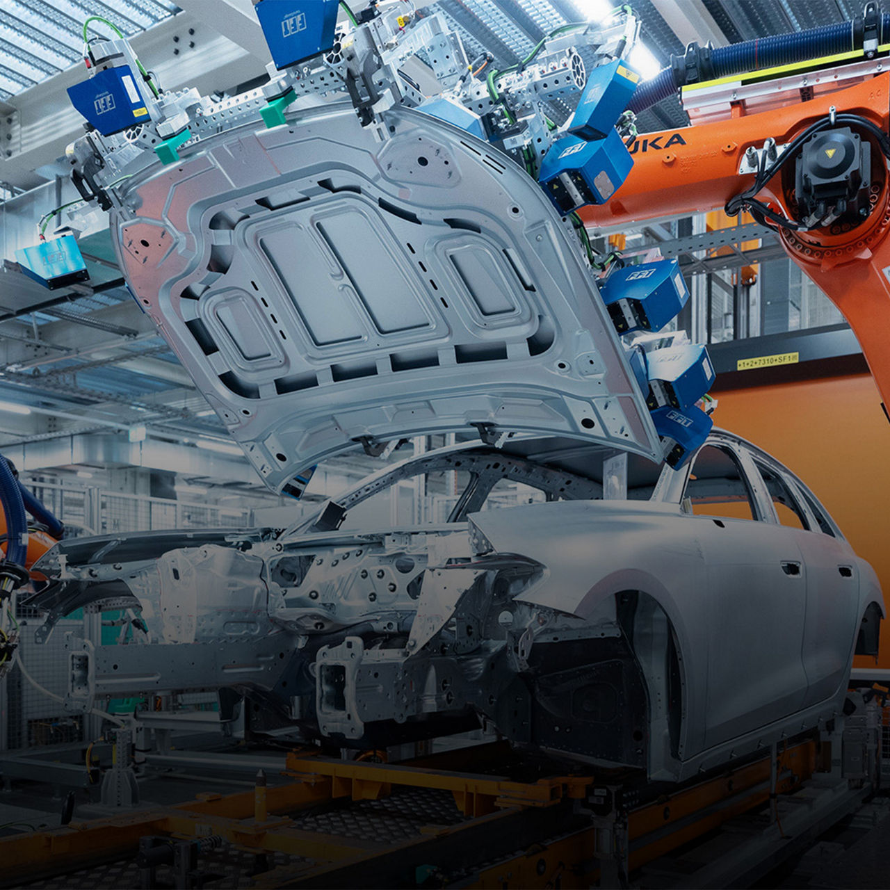 A production robot lifts the body of a car in a modern production hall. The scene shows advanced automation technology and industrial design.