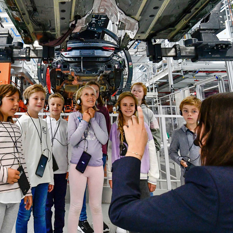 Kinder betrachten bei einer Führung die Karosserie eines Audi von unten.