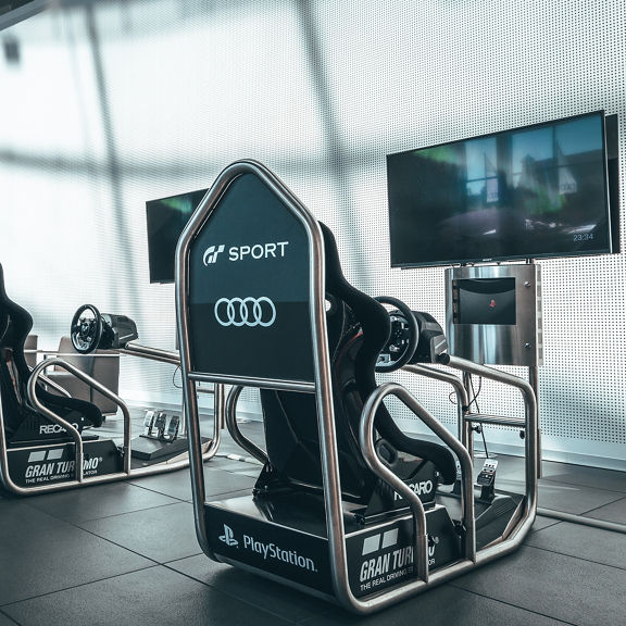 Two Audi racing simulators with steering wheels and monitors in a modern room with Audi branding.