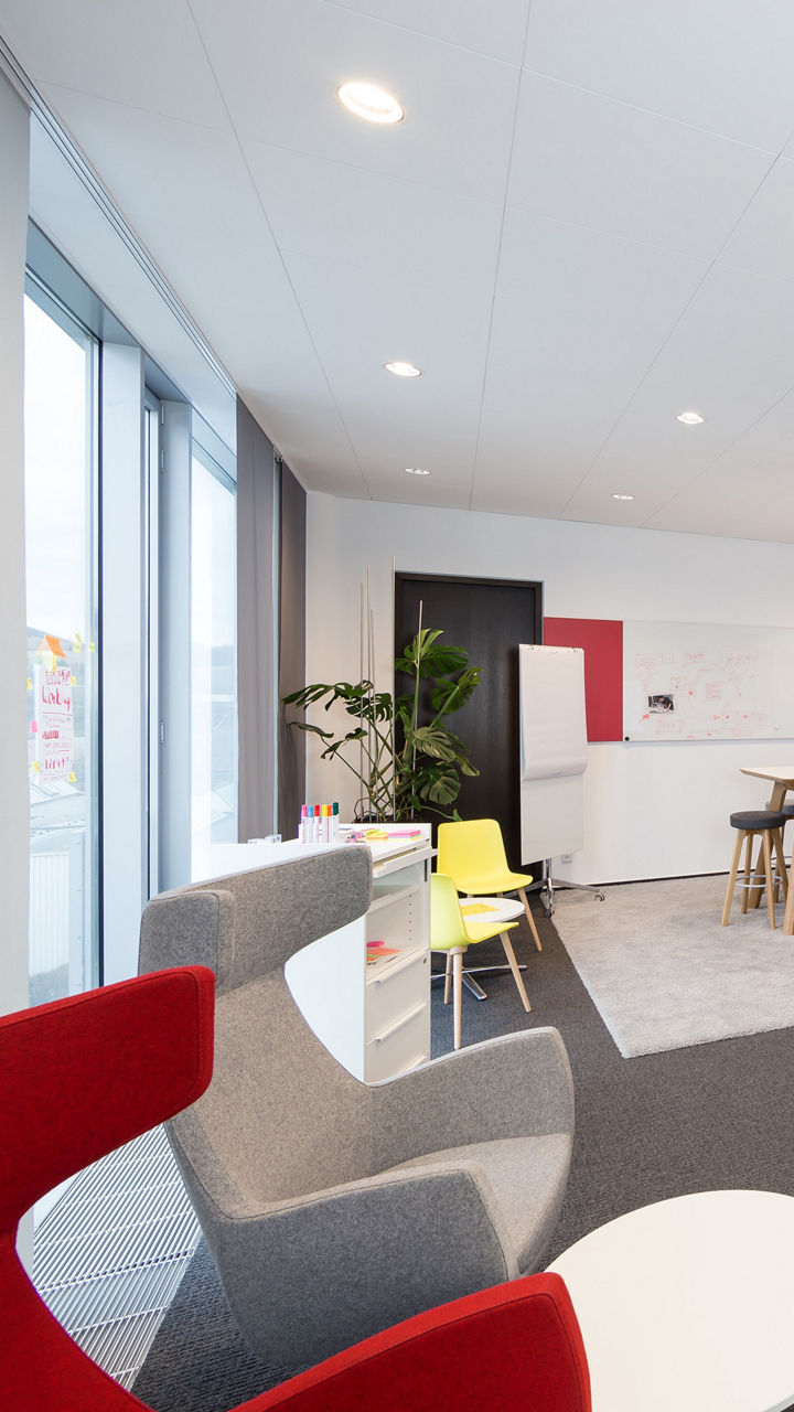 A modern creative space with colourful stools, a standing bar with stools, whiteboards on the walls and a small kitchenette with drinks. The room is bright and inviting, with cosy seating areas and accessories for brainstorming and meetings.