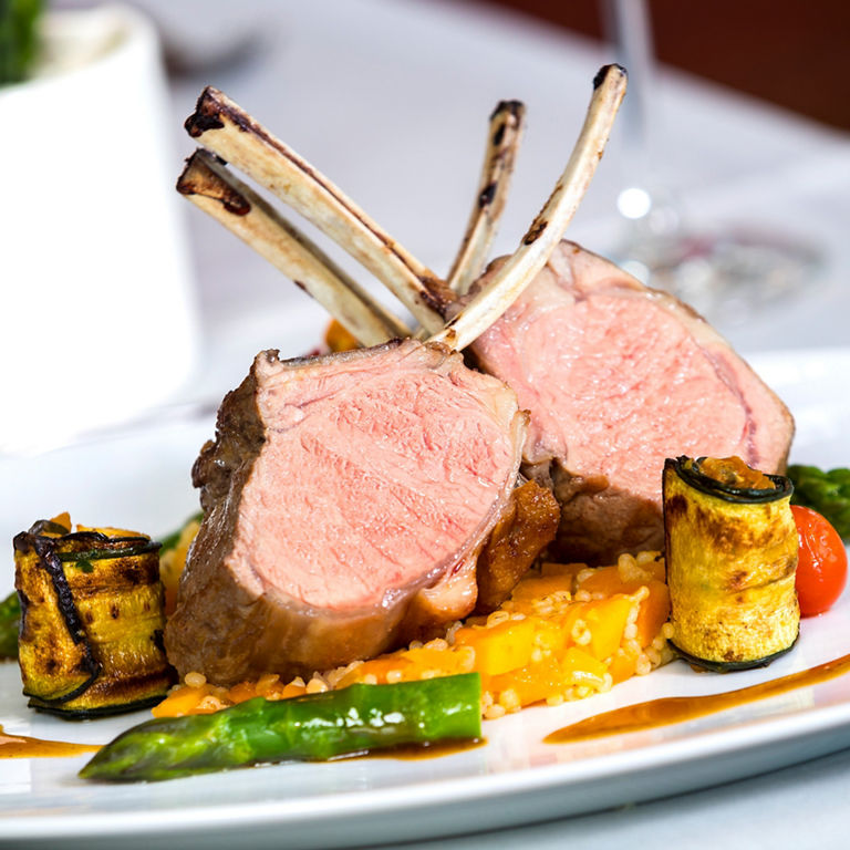 A plate of lamb chops, accompanied by grilled vegetables, asparagus and a sauce, skilfully arranged.