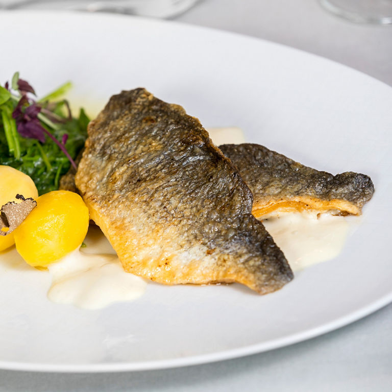 A dish with fried fish fillet, small potatoes, truffle slices and a fresh side salad.