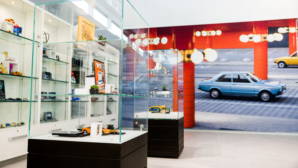 A room with glass cabinets displaying model cars and other collector's items. A wall with a picture of classic cars can be seen in the background.