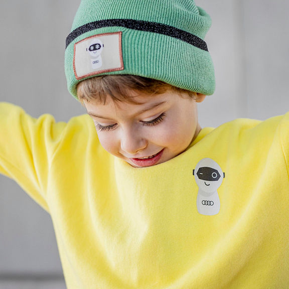 After shot of a child, arms outstretched, wearing a yellow ADUI Kids sweater and green beanie.