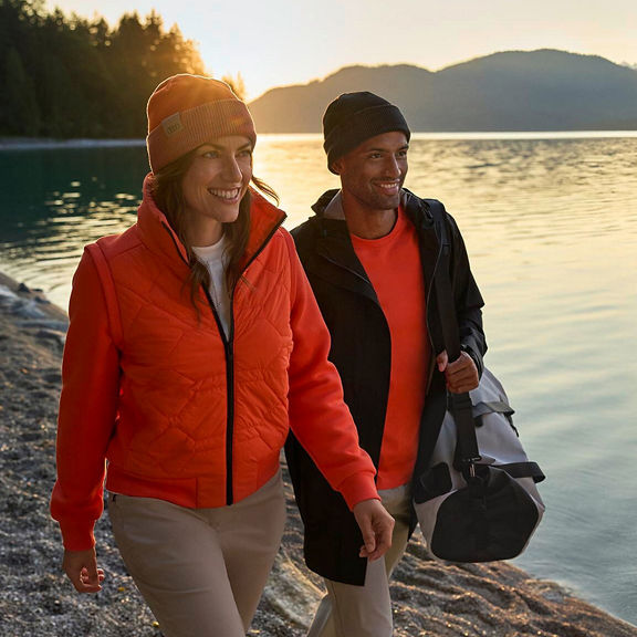 A man and a woman carrying products from the Audi collection and walking along a riverbank.