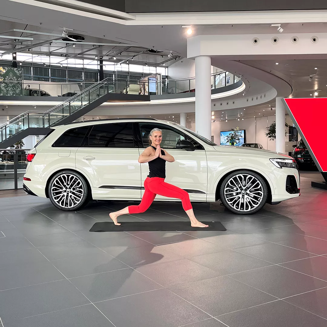 Eine Frauen steht im Foyer des Audi Forum Neckarsulm in einer Yoga-Pose vor einem Audi-Modell.