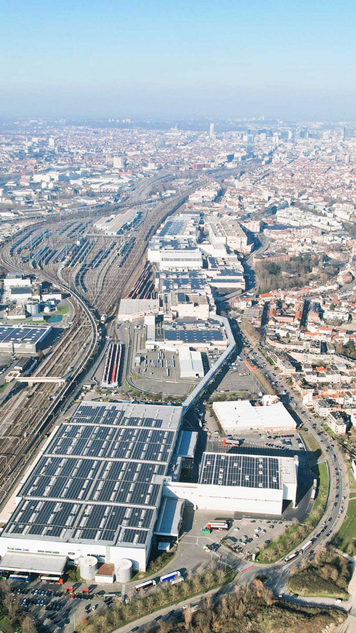 Vue aérienne de l'usine Audi Brussels. Un grand bâtiment avec des panneaux solaires sur le toit, à droite, longe la voie ferrée.