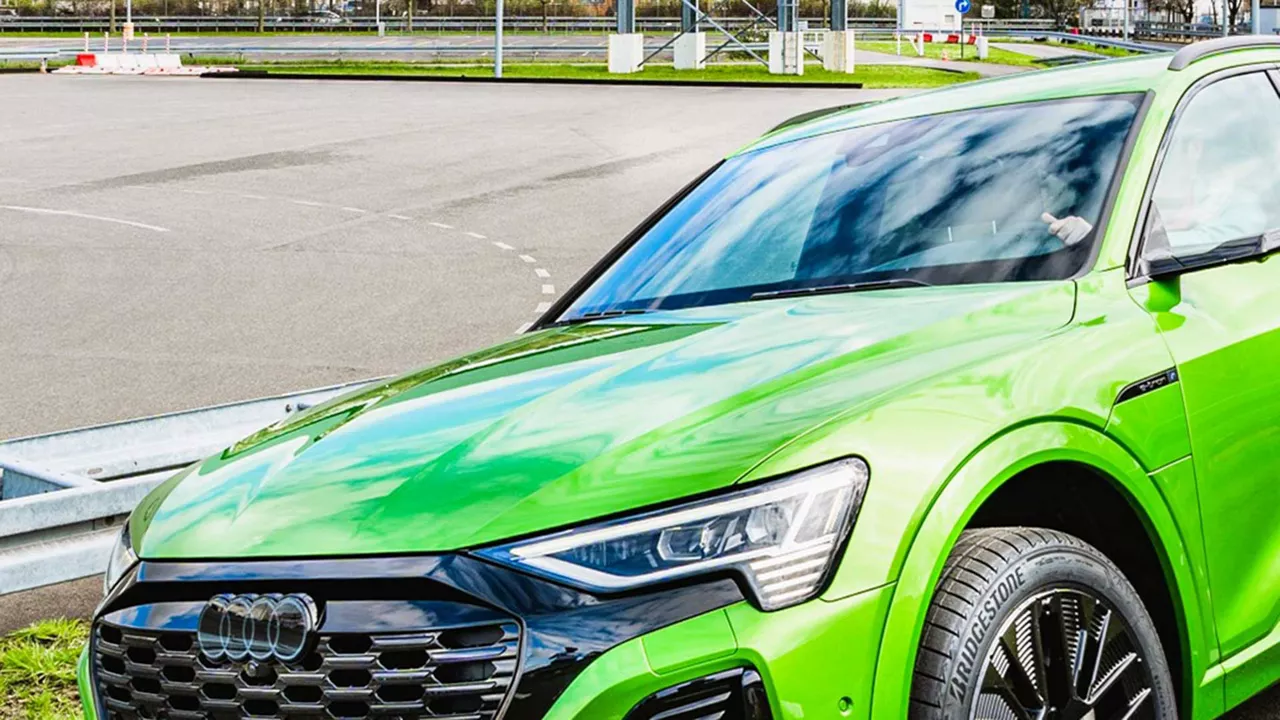 A green Audi Q8 e-tron in a side frontal shot while driving. A race track can be seen in the background