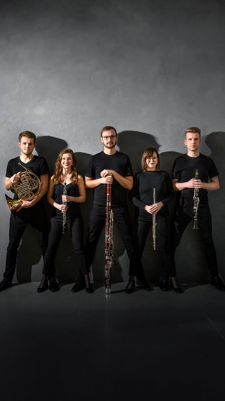Fünf Mitglieder des Alinde Quintet stehen nebeneinander vor grauer Wand, jeweils mit ihrem Blasinstrument in der Hand.
