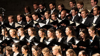 Audi Jugendchorakademie sitzt und singt (Schwarze Gewänder und ein Notenbuch in der Hand)