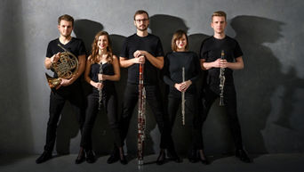 Alinde Quintet (2 Frauen und 3 Männer) steht in schwarzen Outfit vor einer grauen Wand mit Instrumenten in der Hand