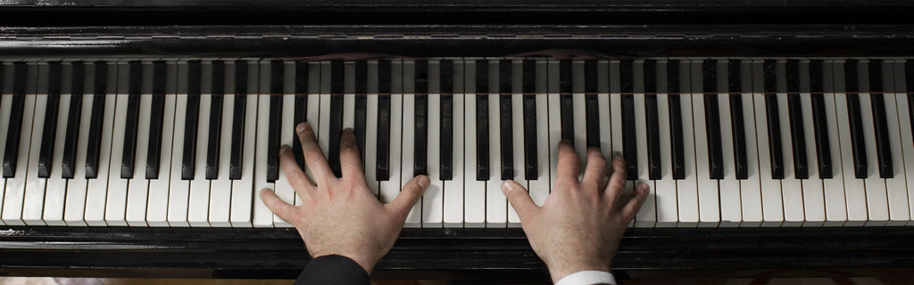 Zwei Hände spielen auf den Tasten eines schwarzen Konzertflügels.