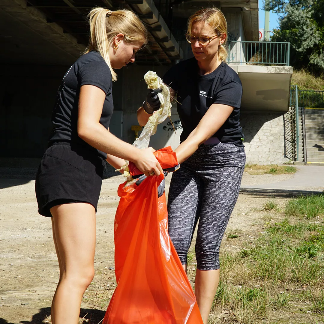 Two women with a red rubbish bag collect rubbish.