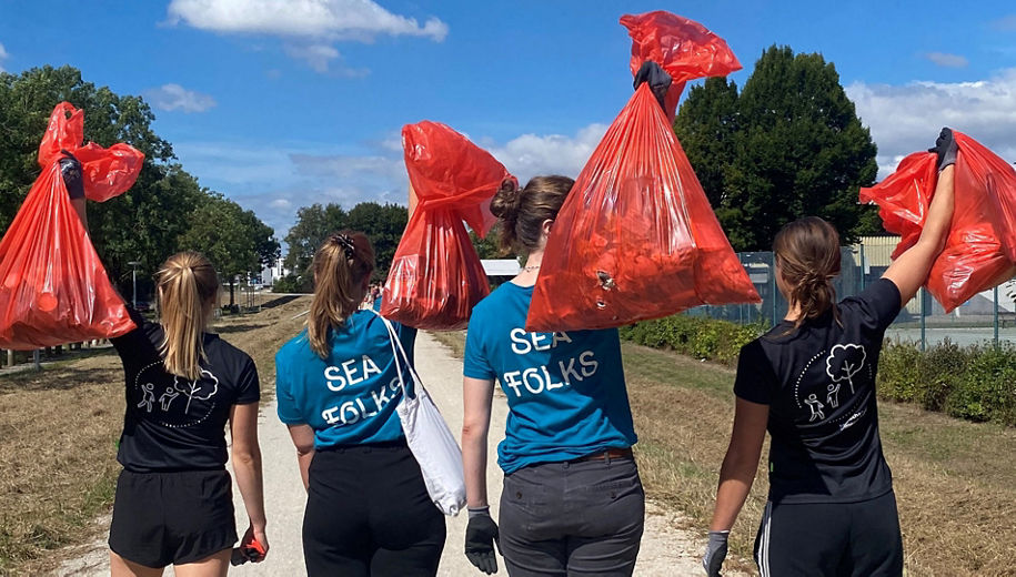 4 teenagers with their backs to the camera lift red rubbish bags filled with rubbish into the air.