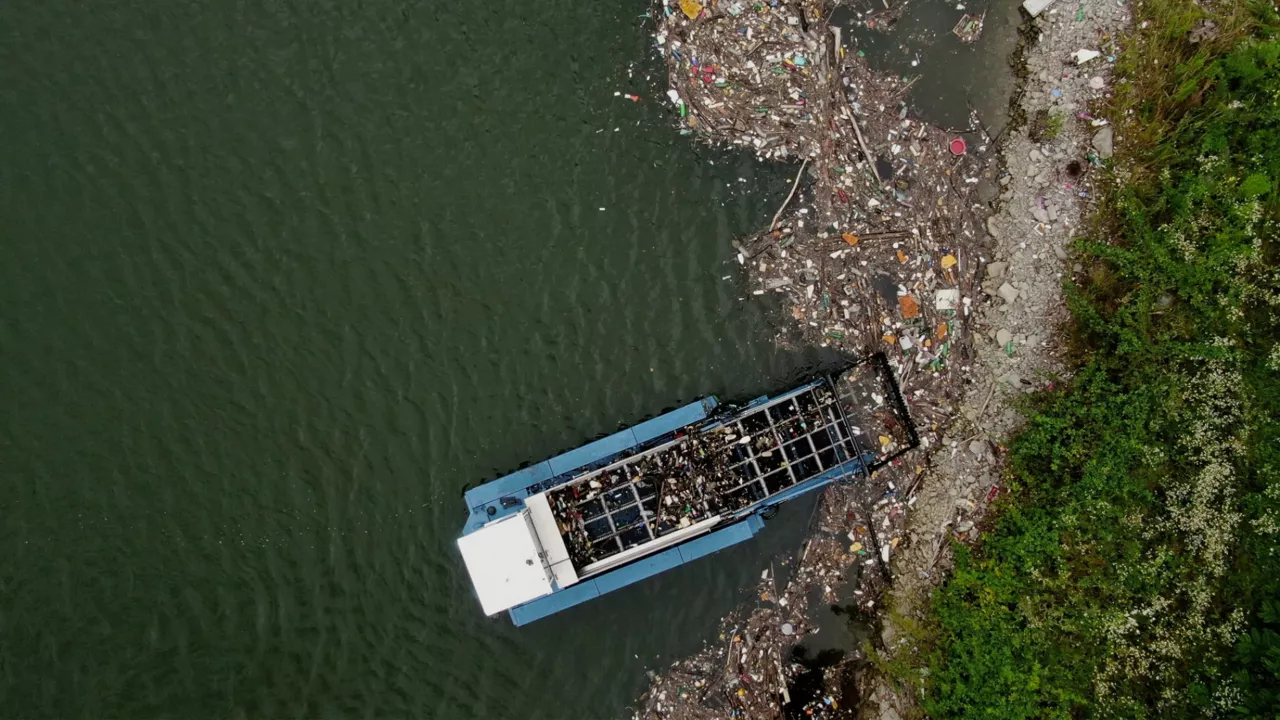 Ein Müllsammelboot von oben an einem Flussufer von Müll umgeben.