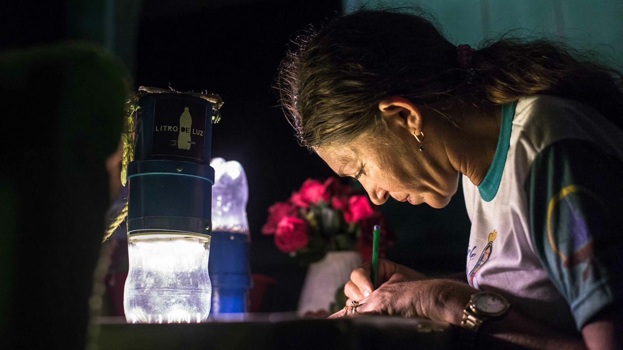 Old woman works on a desk. A light source spends light.