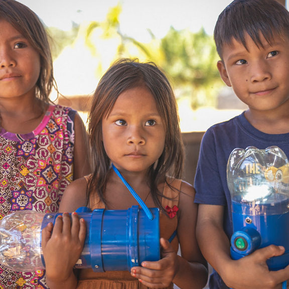 3 children stand together and hold two solar lamps in their hands.