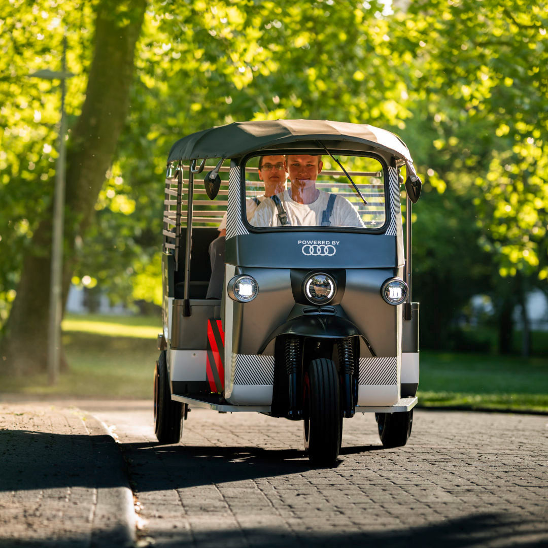 Eine E-Rikscha fährt auf einer mit Bäumen umsäumten Kopfsteinpflasterstrasse.