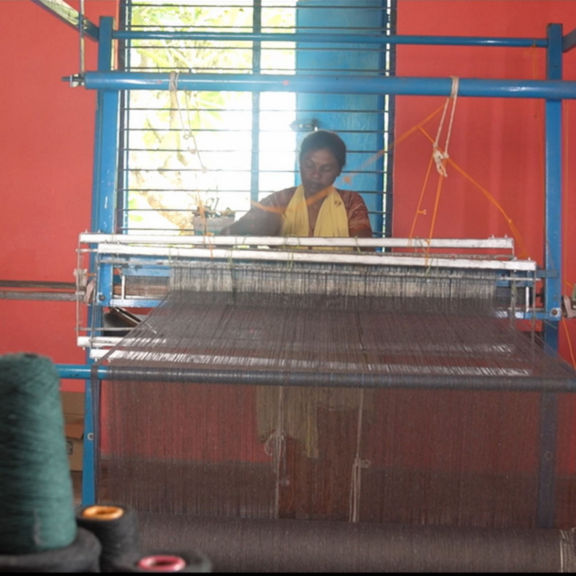 A woman sits behind a loom and weaves.