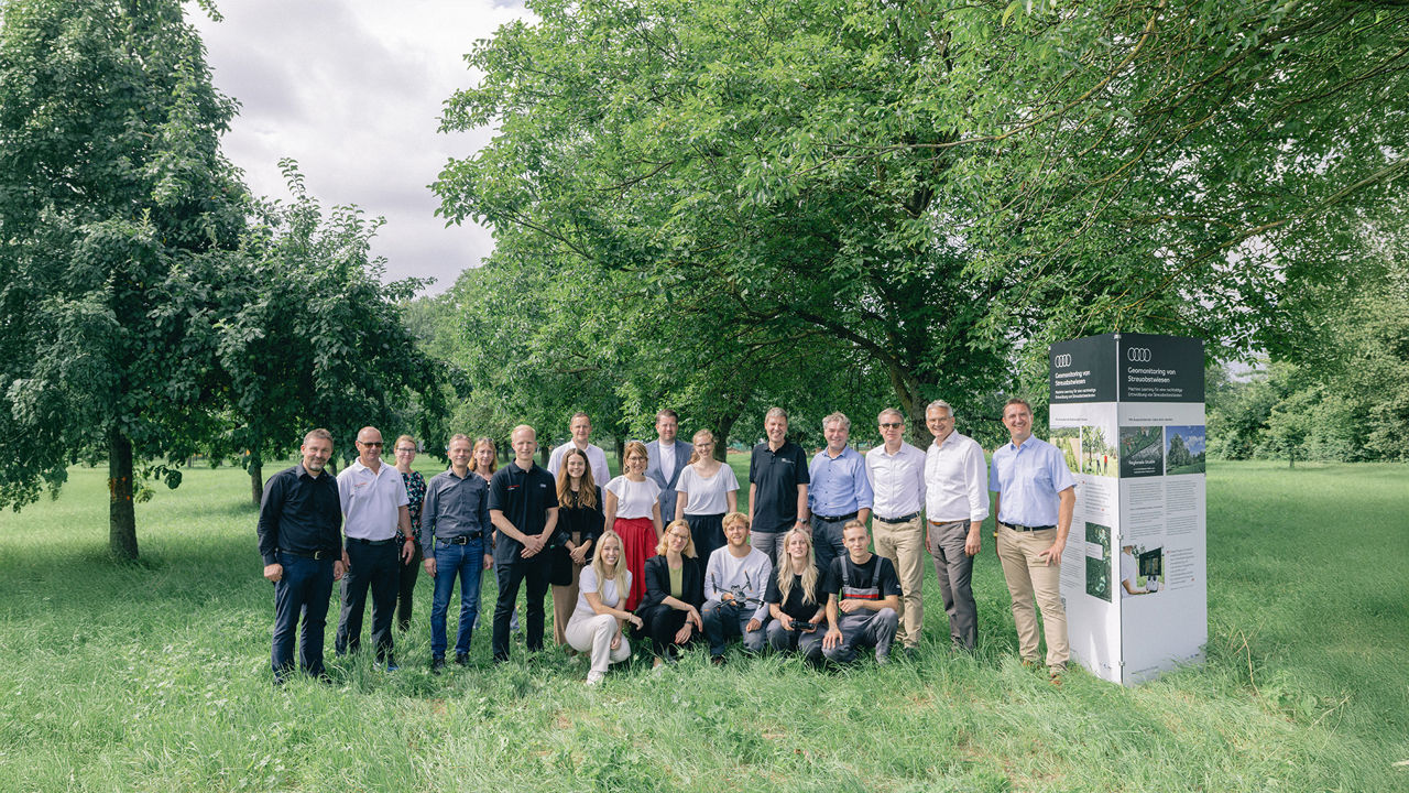 Gruppe von 20 Personen steht auf einer Streuobstwiese neben einer Infotafel und blickt gemeinsam in die Kamera.