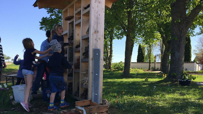 Children look at a wooden structure outdoors