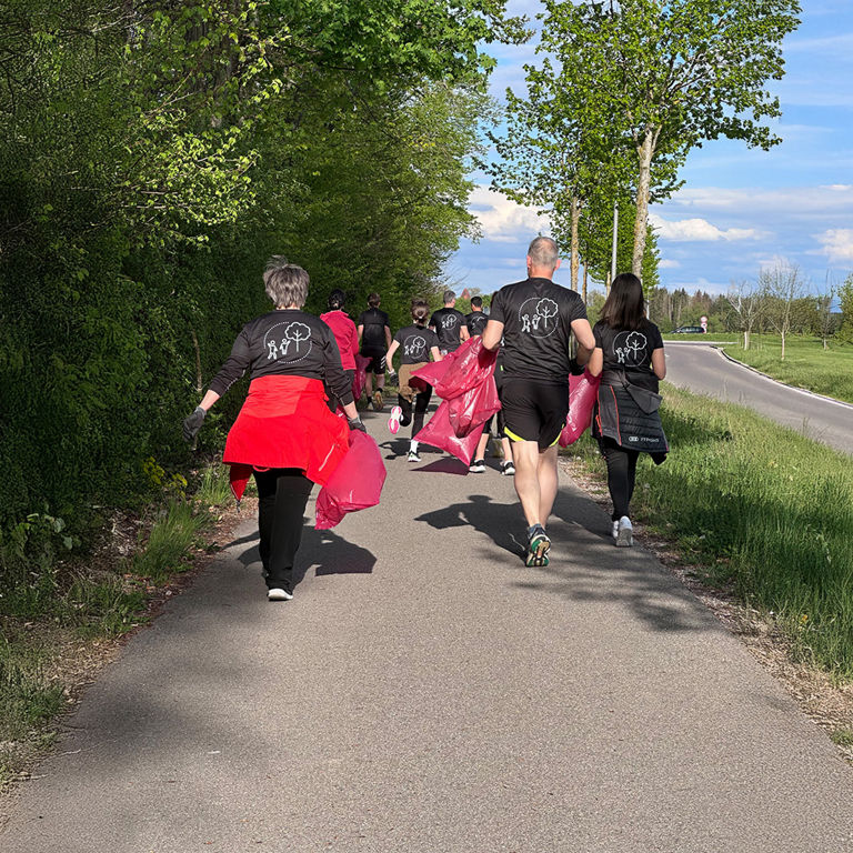 People running along a path with pink trash bags during a litter cleanup event in a green rural area.