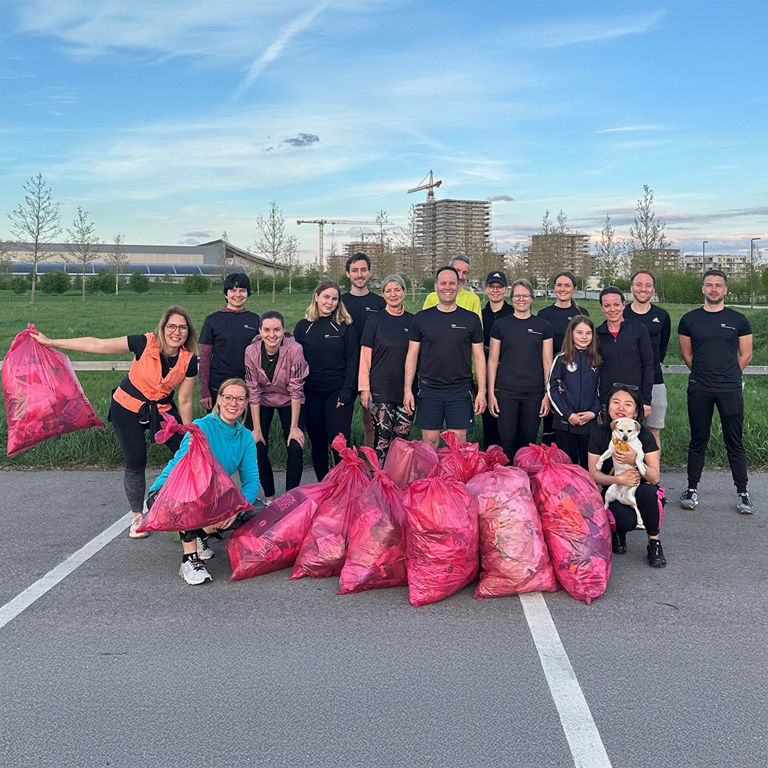 Group of people outdoors posing with multiple full pink trash bags after cleanup, one person holding a small dog.