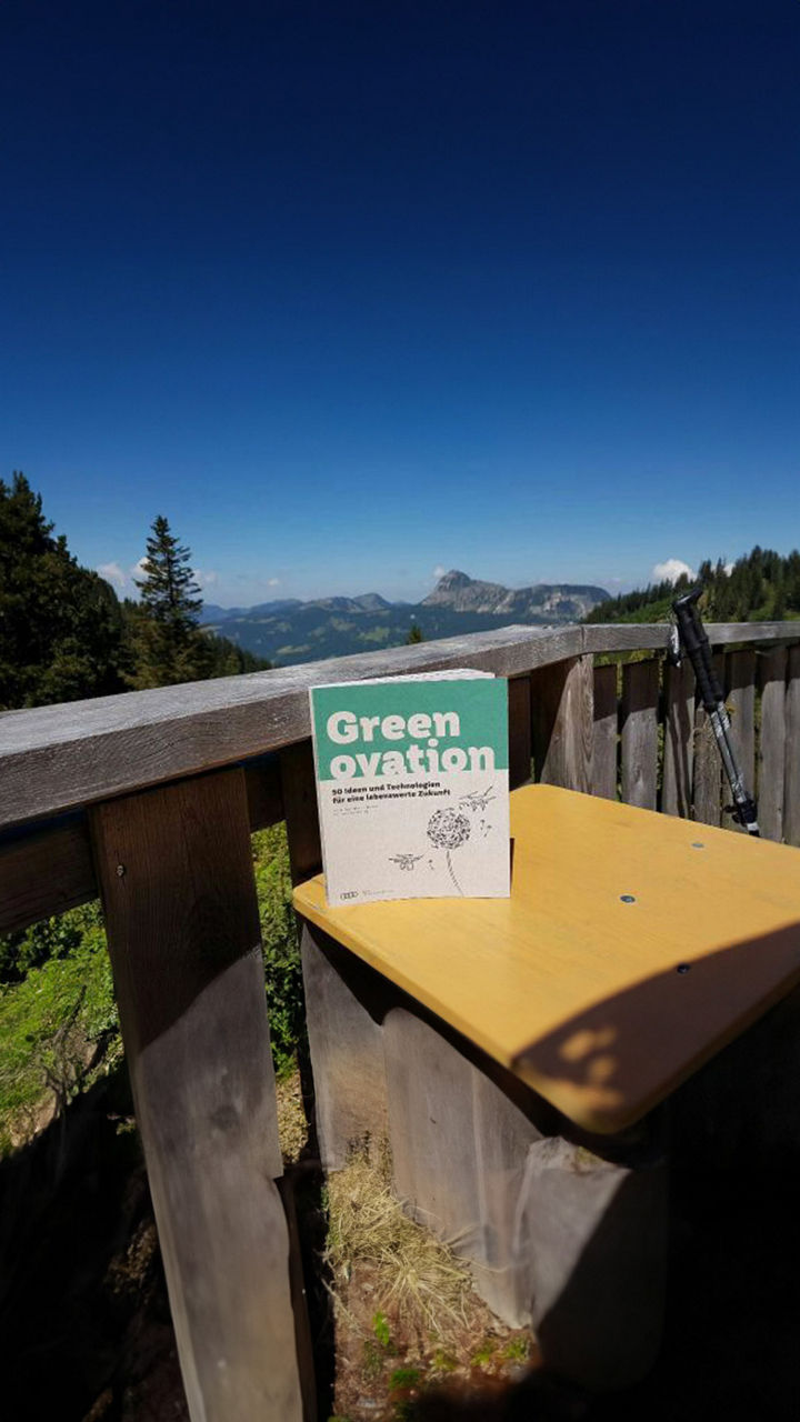 A book on sustainable innovations stands on a wooden table with a mountain panorama in the background