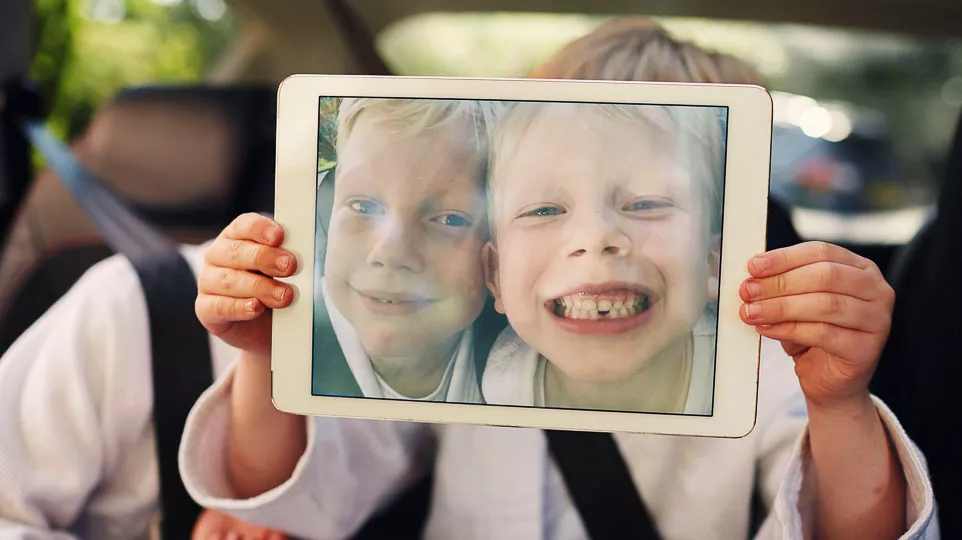 Two boys proudly display a tablet showing a picture of themselves, smiling and enjoying the moment together