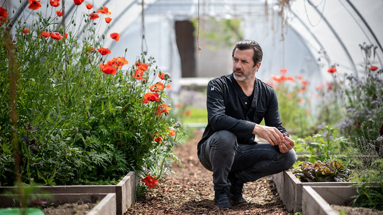 Andreas Caminada neben mehreren Beeten mit Blumen darin