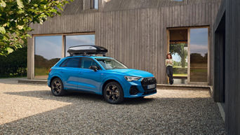 Audi mit Dachbox vor Haus mit Frau