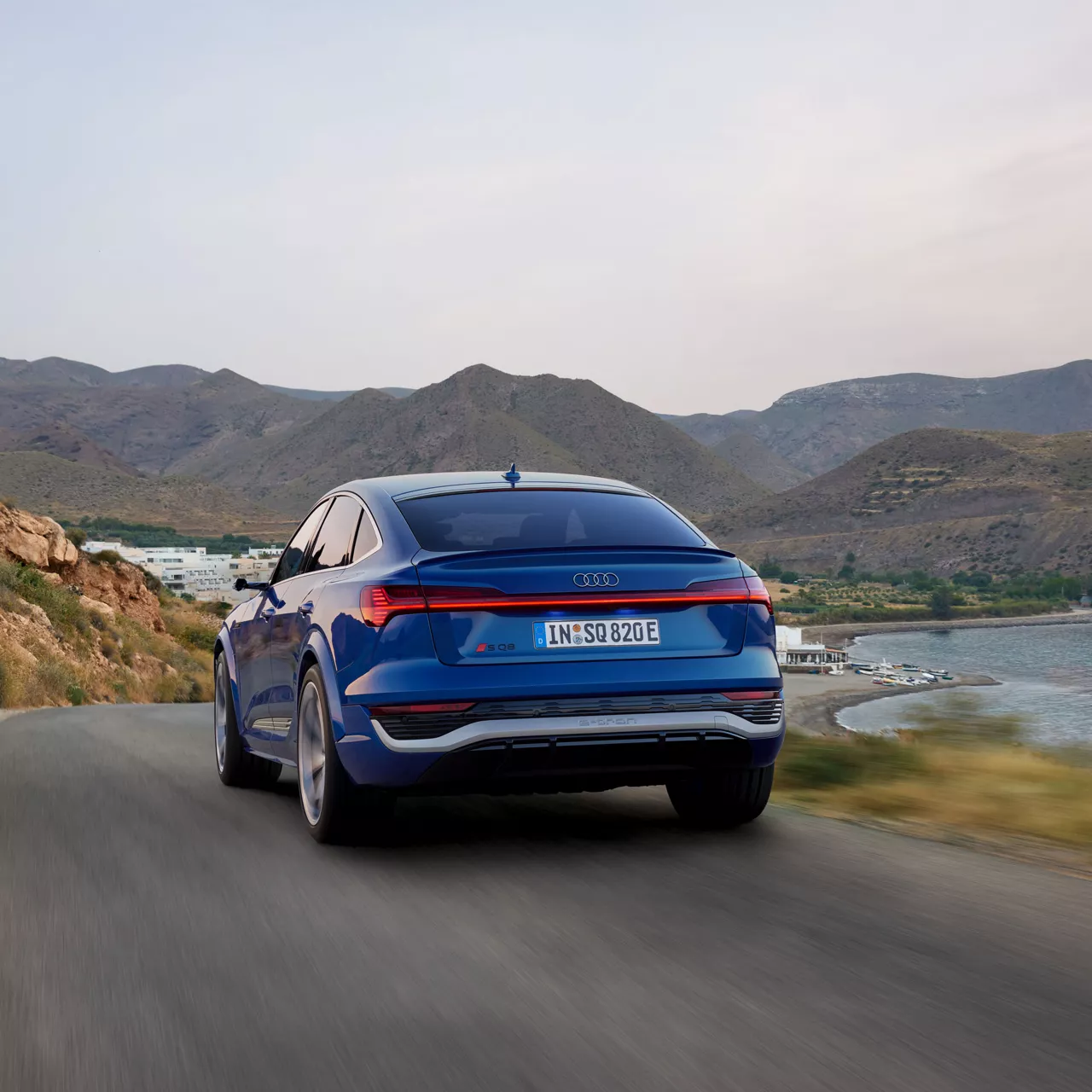 Ein blauer Audi fährt auf einer Straße am Wasser