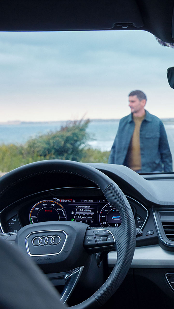 Frau sitzt auf dem Beifahrersitz eines Audi, durch die Windschutzscheibe sieht man einen verschwommenen Mann auf das Auto zugehen