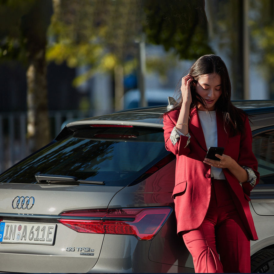 Frau mit Handy in der Hand lehnt an einem Audi A6 TFSIe