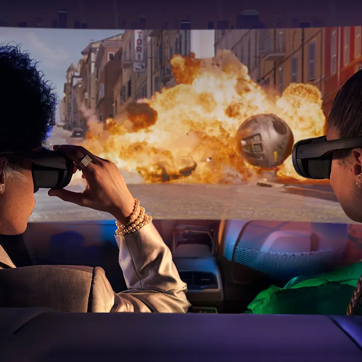 Zwei Personen sitzen mit VR Brillen in einem Auto und schauen sich eine Explosion an