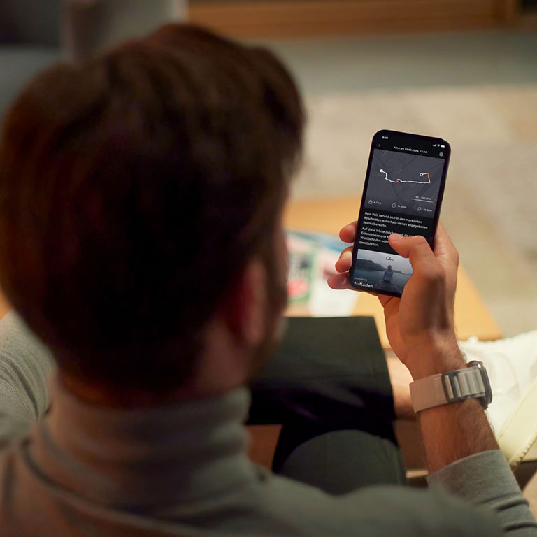 Man holding a cell phone with which he is looking at the Audi activ coach