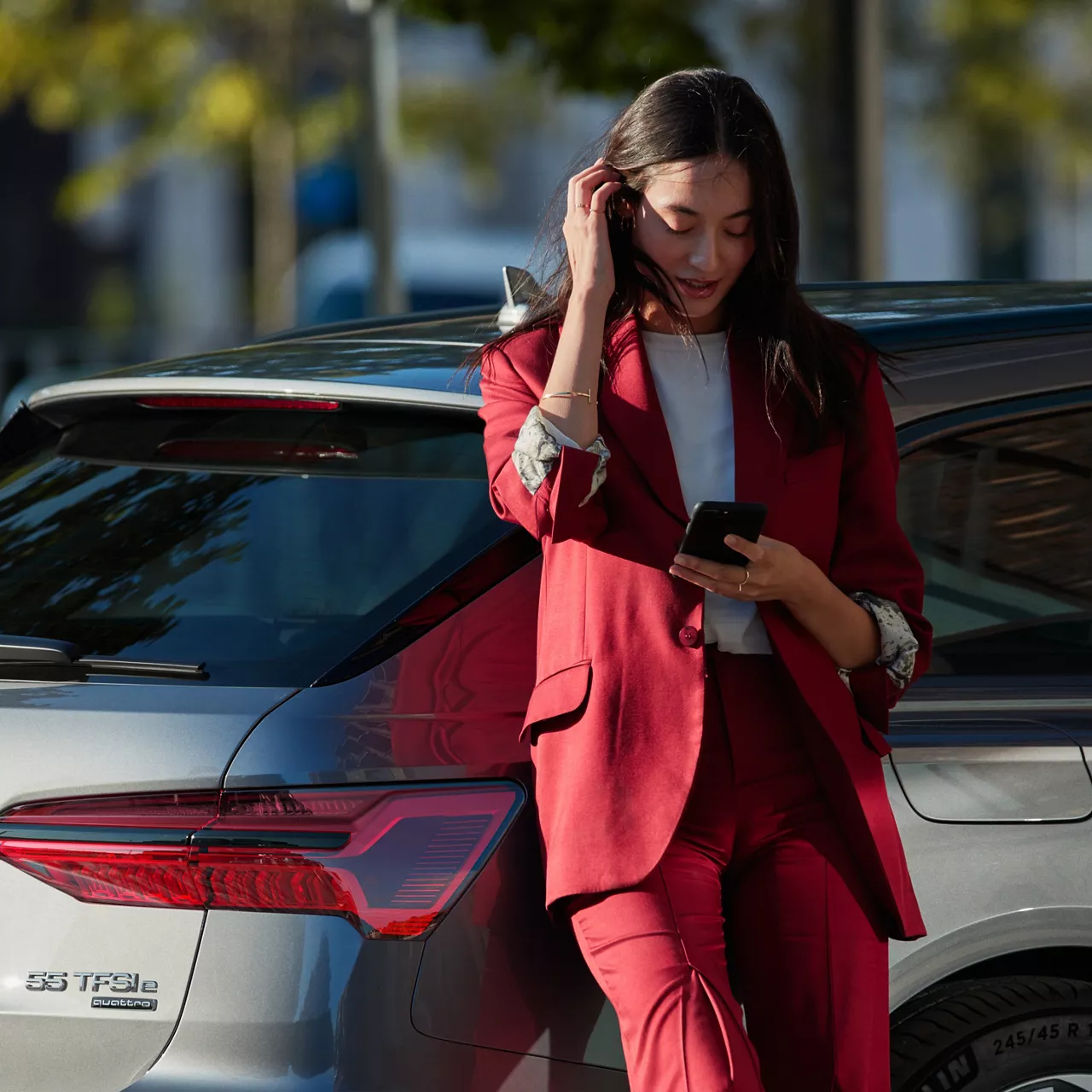 Frau lehnt an einem Audi, hält dabei ein Handy in der Hand