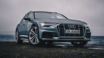 Grauer Audi auf nasser Straße am Meer bei bewölktem Himmel.