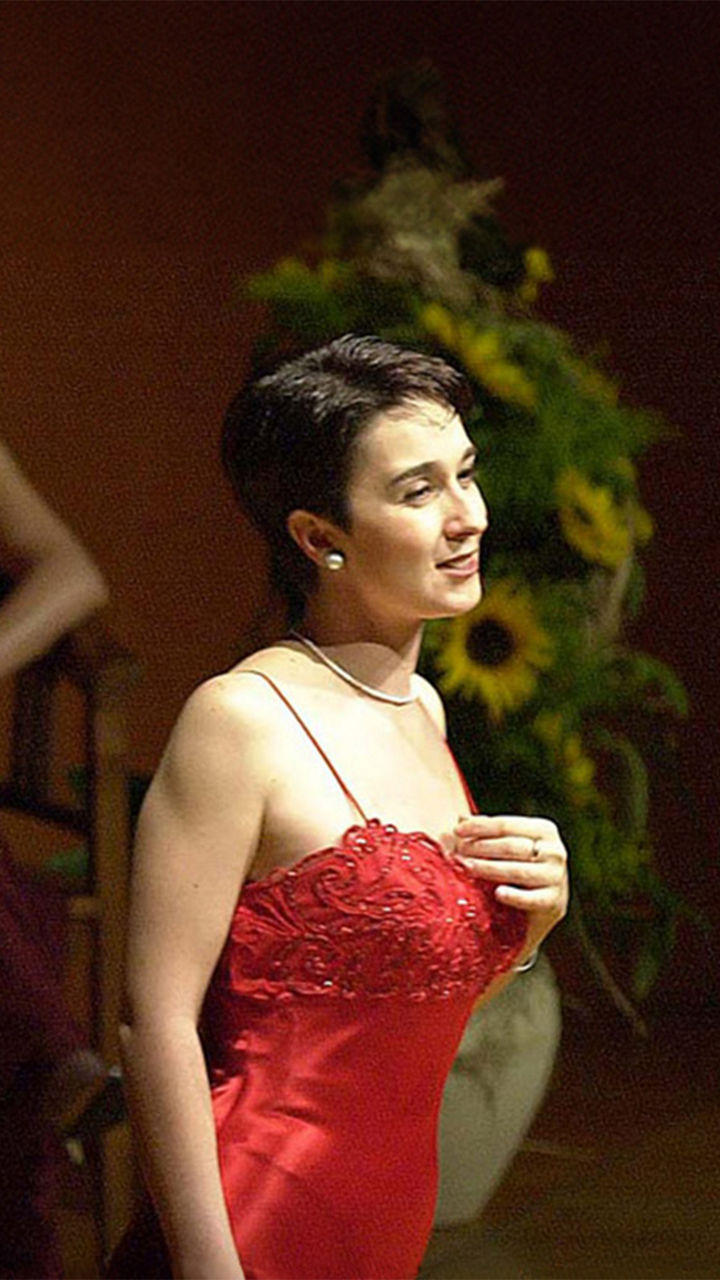 Dunkelhaarige Frau steht im eleganten Abendkleid auf einer Bühne vor einem Piano