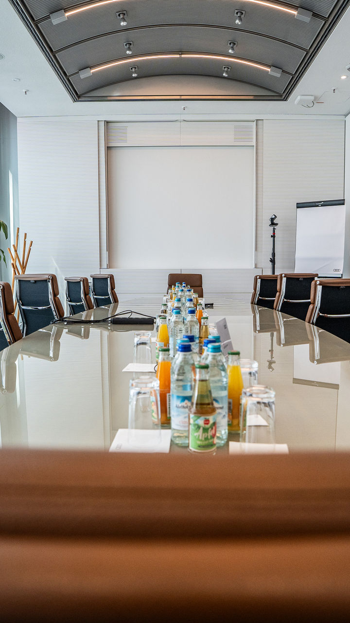 Konferenzraum mit Lederstühlen. Getränke stehen auf dem Tisch. Am Kopfende befindet sich ein FlipChart